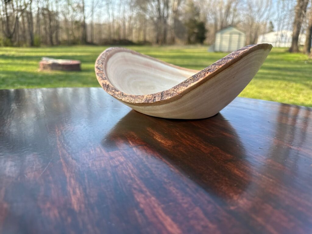 This stunning natural wooden bowl features a gracefully curved design and a unique bark edge that highlights its organic craftsmanship. Perfect for rustic or farmhouse decor